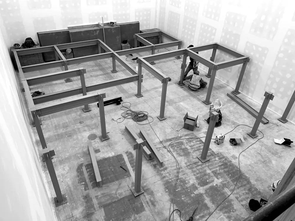 The steel frame of the seating riser under construction, with installers working at floor level
