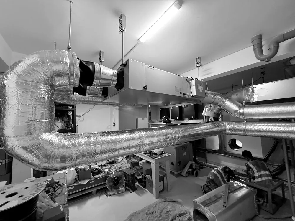 HVAC plant room during installation, with insulated ductwork and an air handling unit, and installers working below