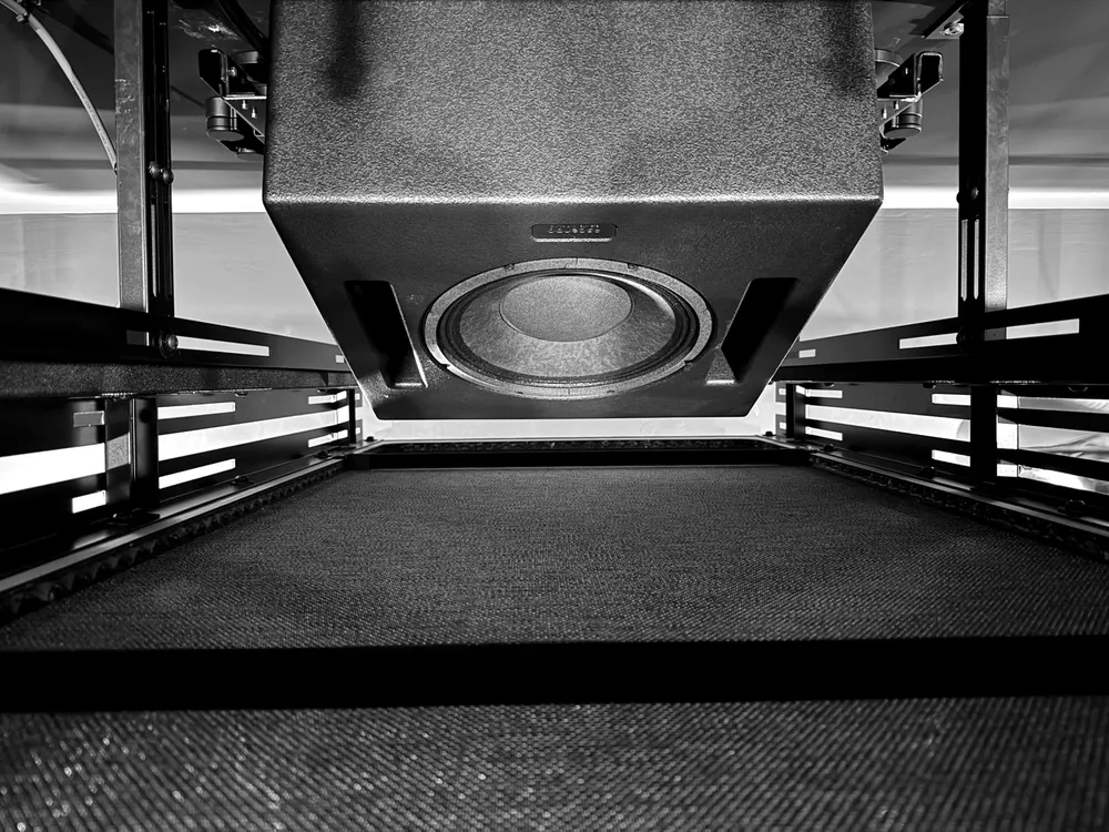 An Ascendo Pro 12 overhead loudspeaker seen from below, hanging from the ceiling structure on the bespoke dual V120 mount