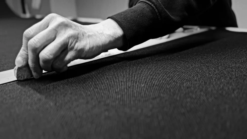 A craftsman marking out acoustic fabric by hand against a straight edge